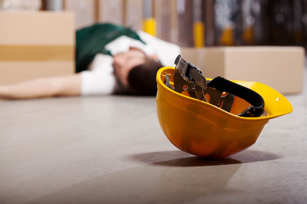 a man at work injured laying on the floor with a yellow hard hat nearby.